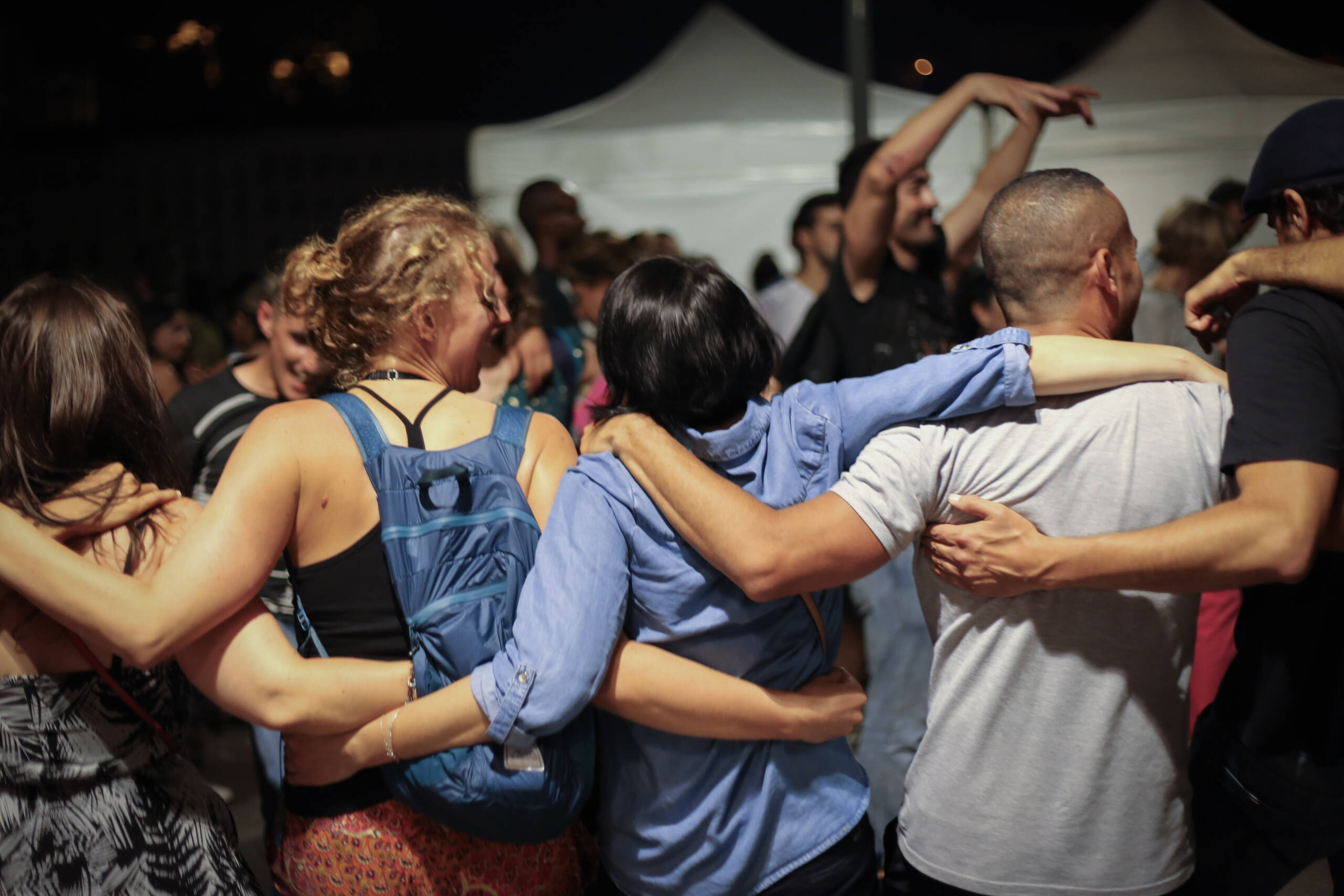 Four people linked arm in arm at a night festival, all photographed from behind